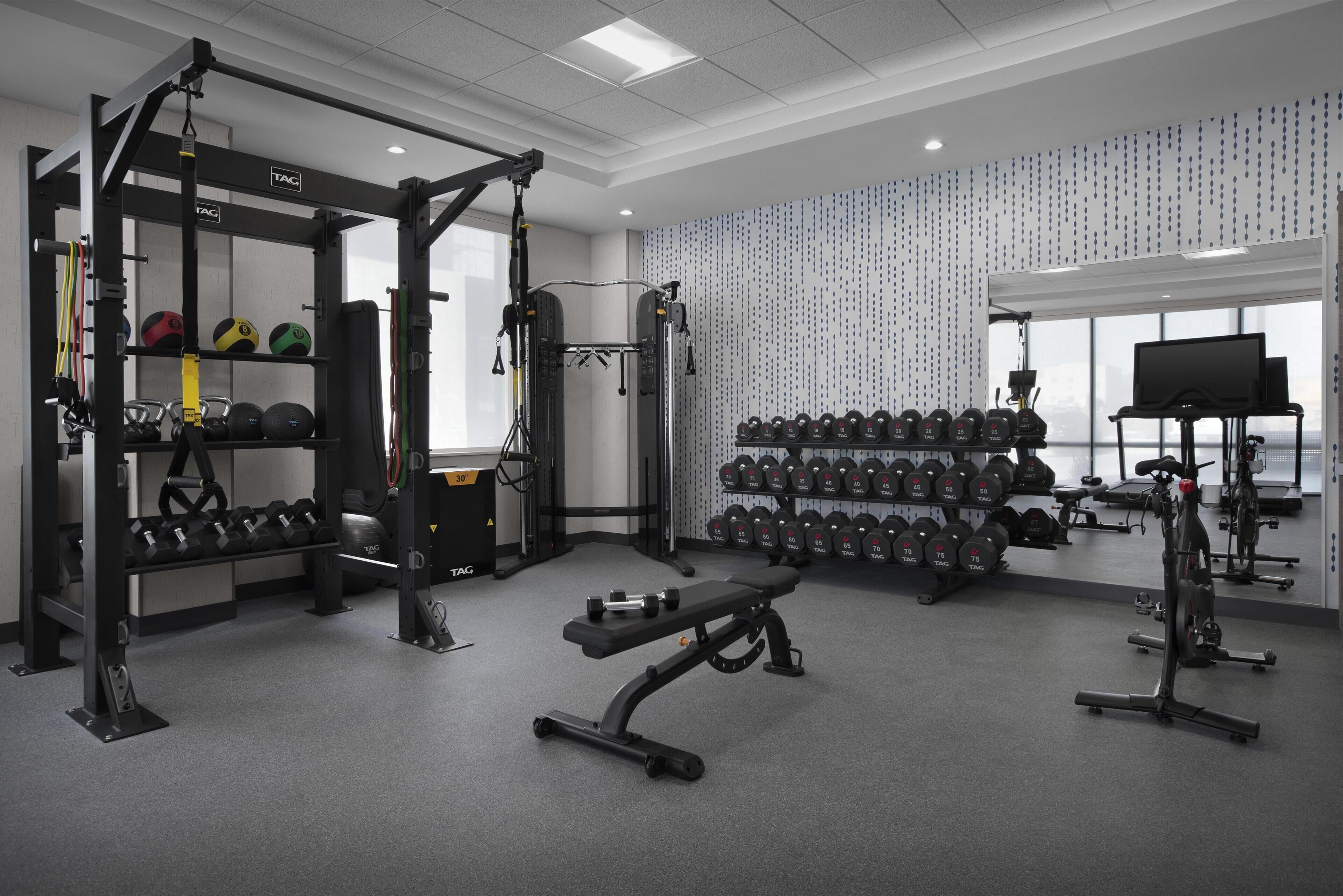 A gym with weightlifting equipment, dumbbells, and a bench.