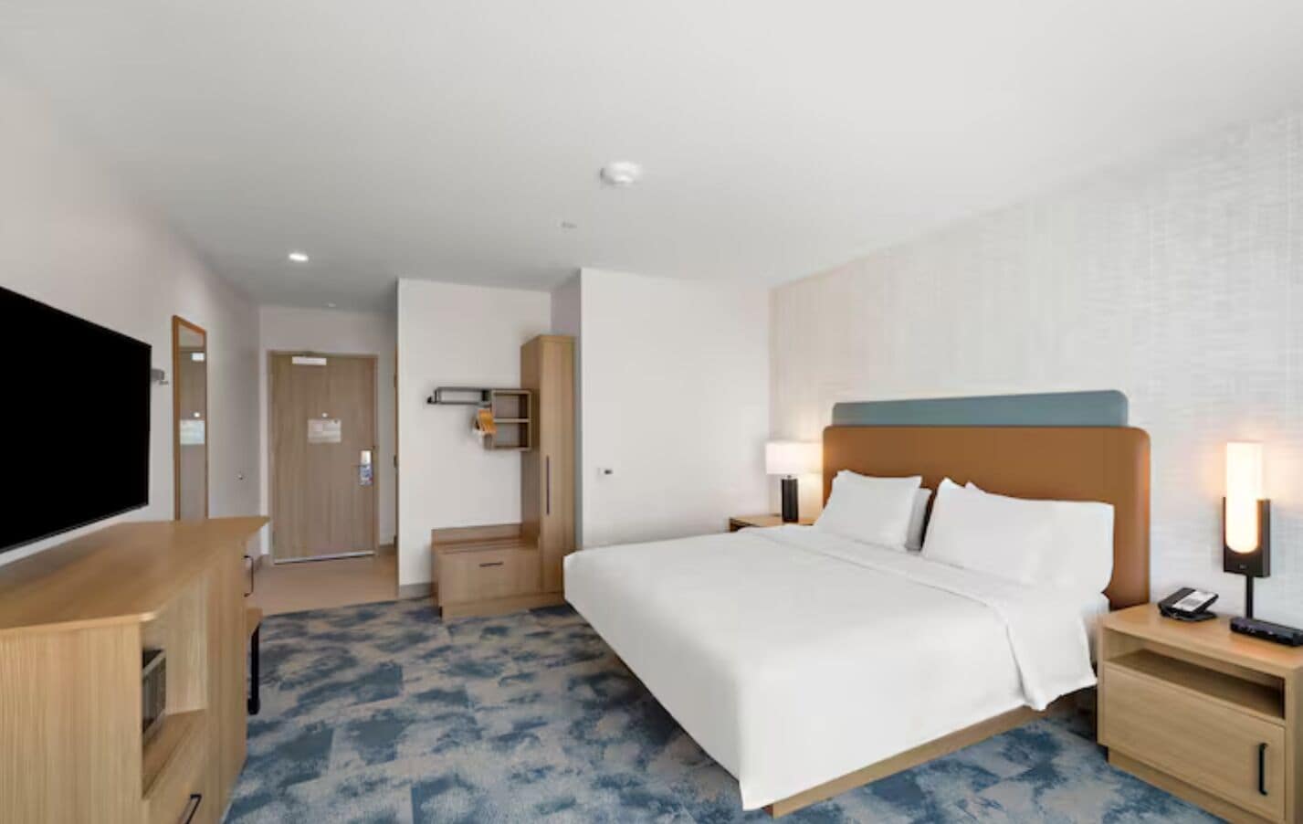 A hotel room with a bed, bedside tables, a TV, and a wardrobe.