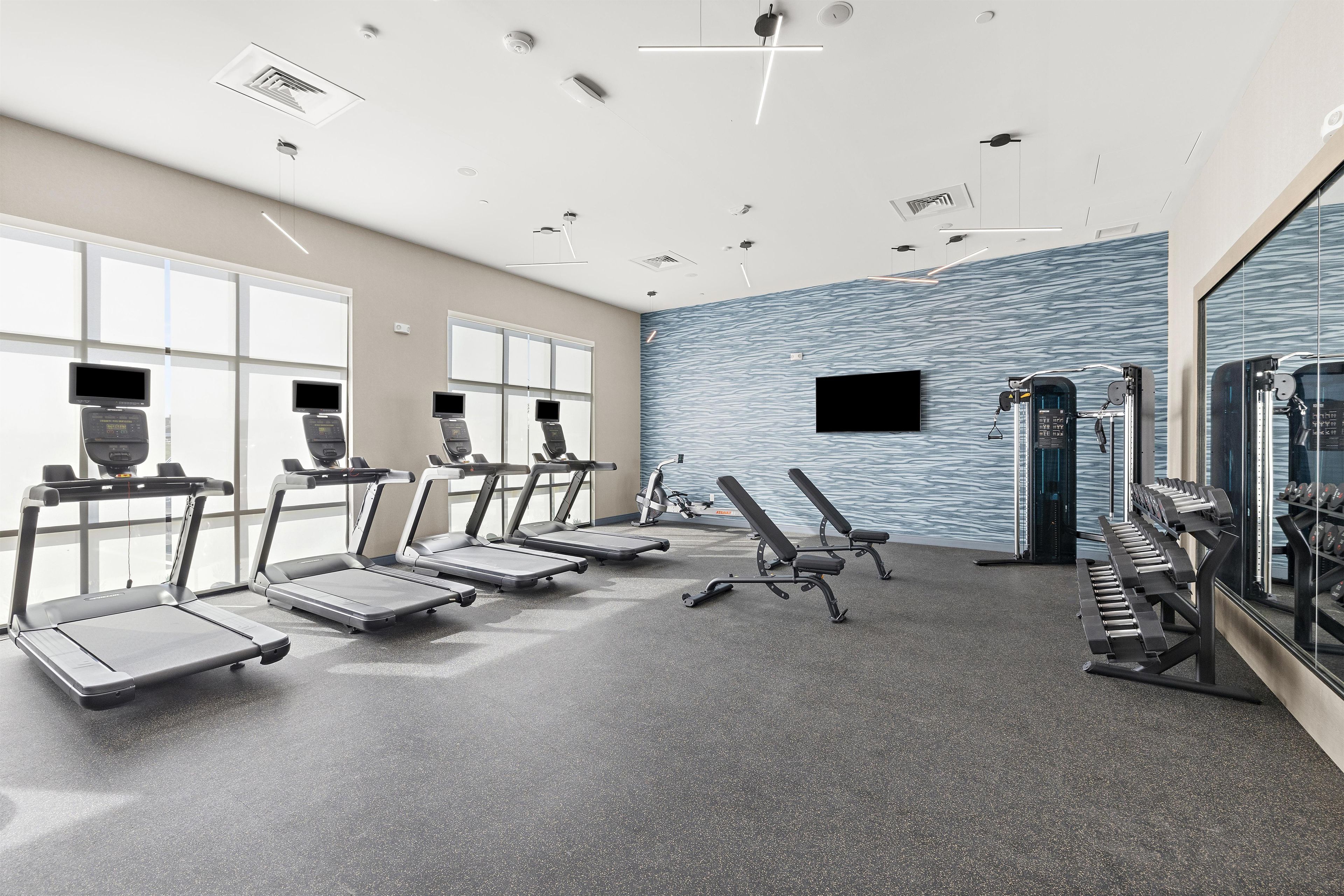 Une salle de sport équipée de tapis de course, de bancs de musculation et d’autres appareils d’exercice.
