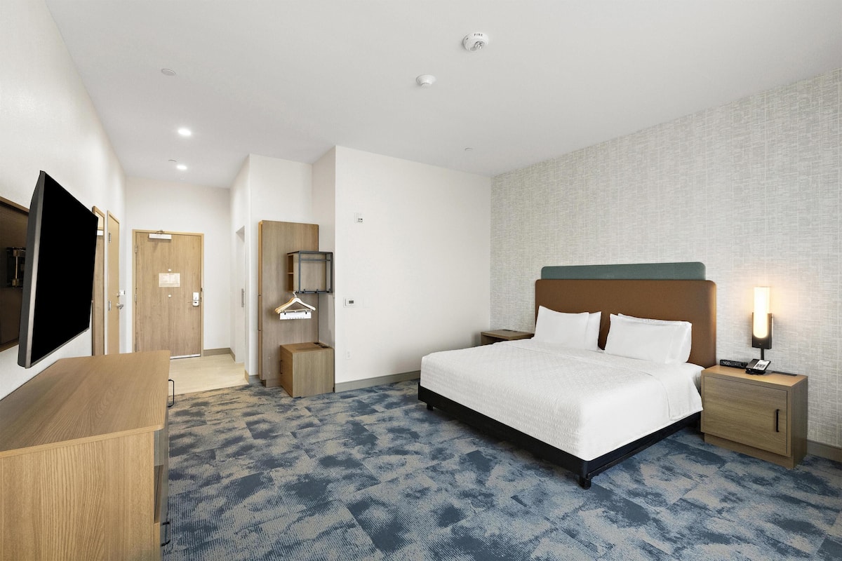 Een hotelkamer met een bed, nachtkastje, lamp, televisie en een kledingkast.