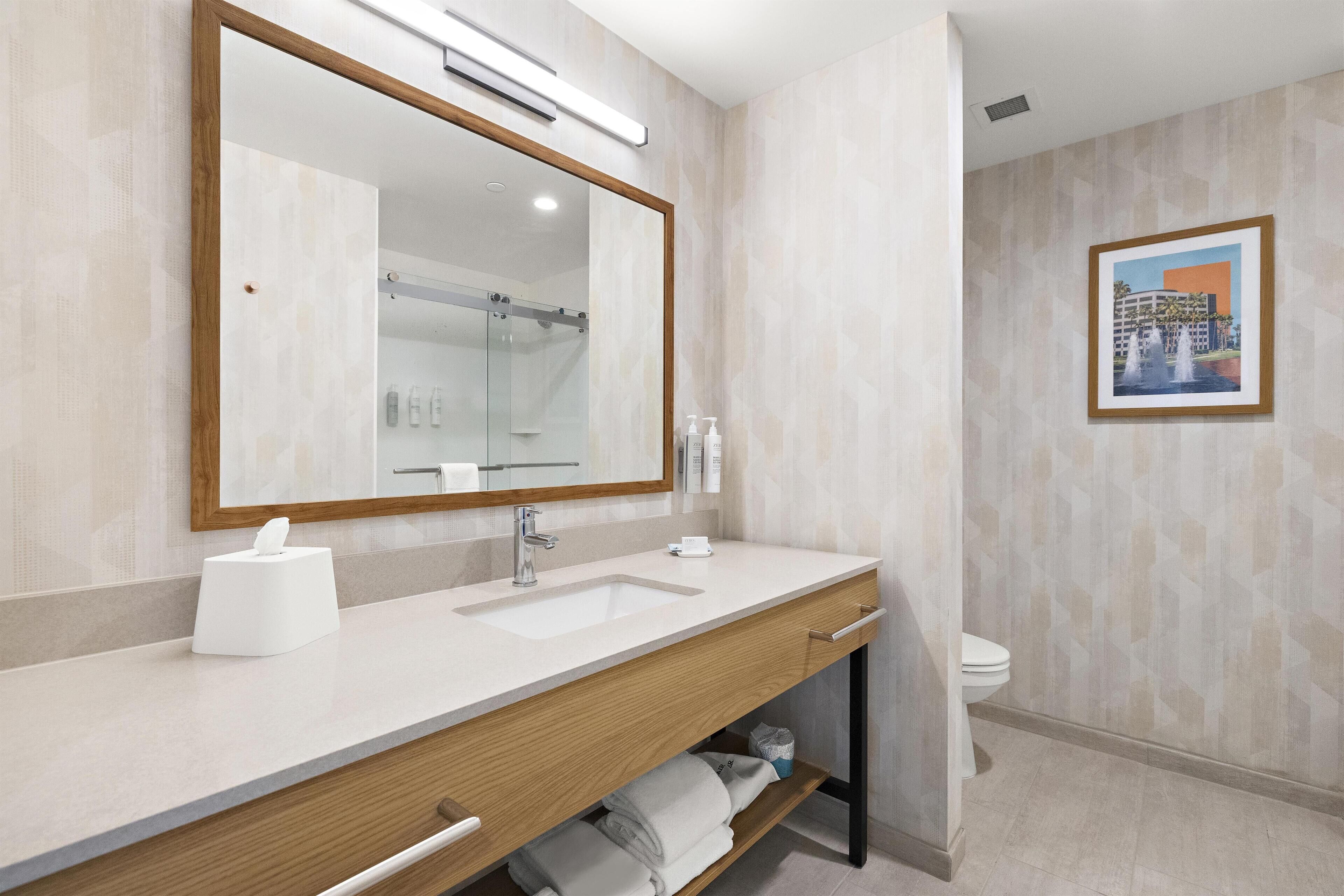 Un baño moderno con un espejo grande, un lavamanos, un inodoro y un cuadro enmarcado en la pared.