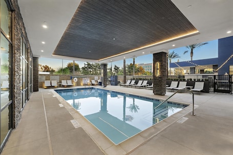 A swimming pool with lounge chairs, a stone wall, and a view of palm trees.