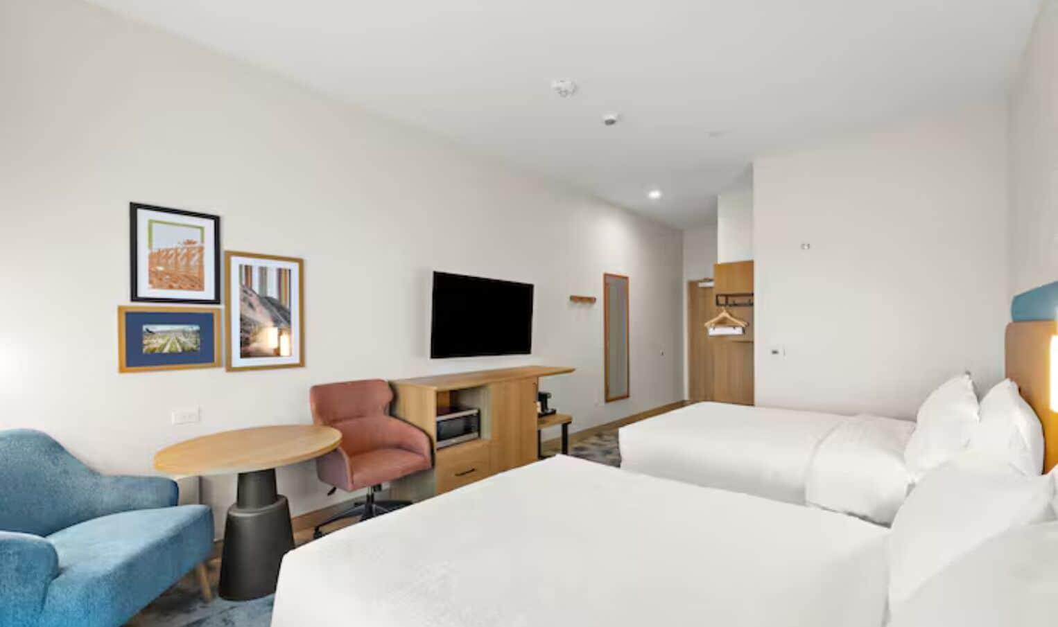 A hotel room with a bed, a desk, a chair, a TV, and framed pictures on the wall.