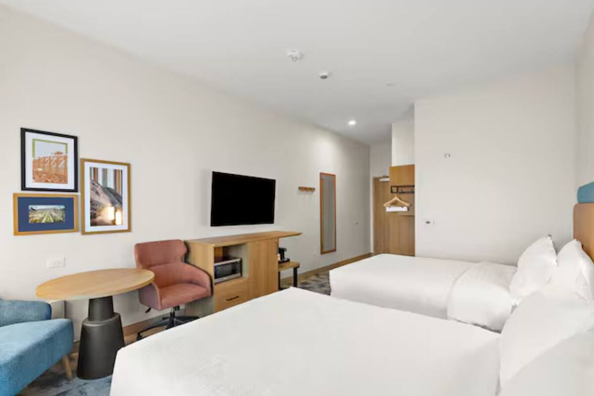 Een hotelkamer met een bed, bureau, stoel, televisie en lijstjes met foto's aan de muur.
