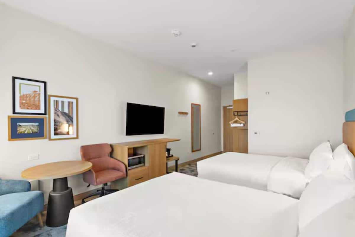 A hotel room with a bed, a desk, a chair, a TV, and framed pictures on the wall.