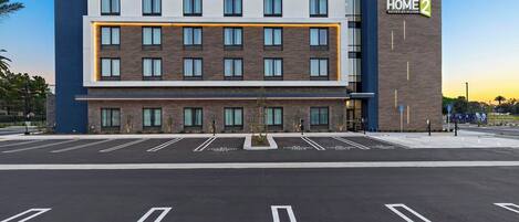 A modern hotel building with multiple floors, a prominent sign for Hampton Inn by Hilton HOME 2, and a parking lot with marked spaces.
