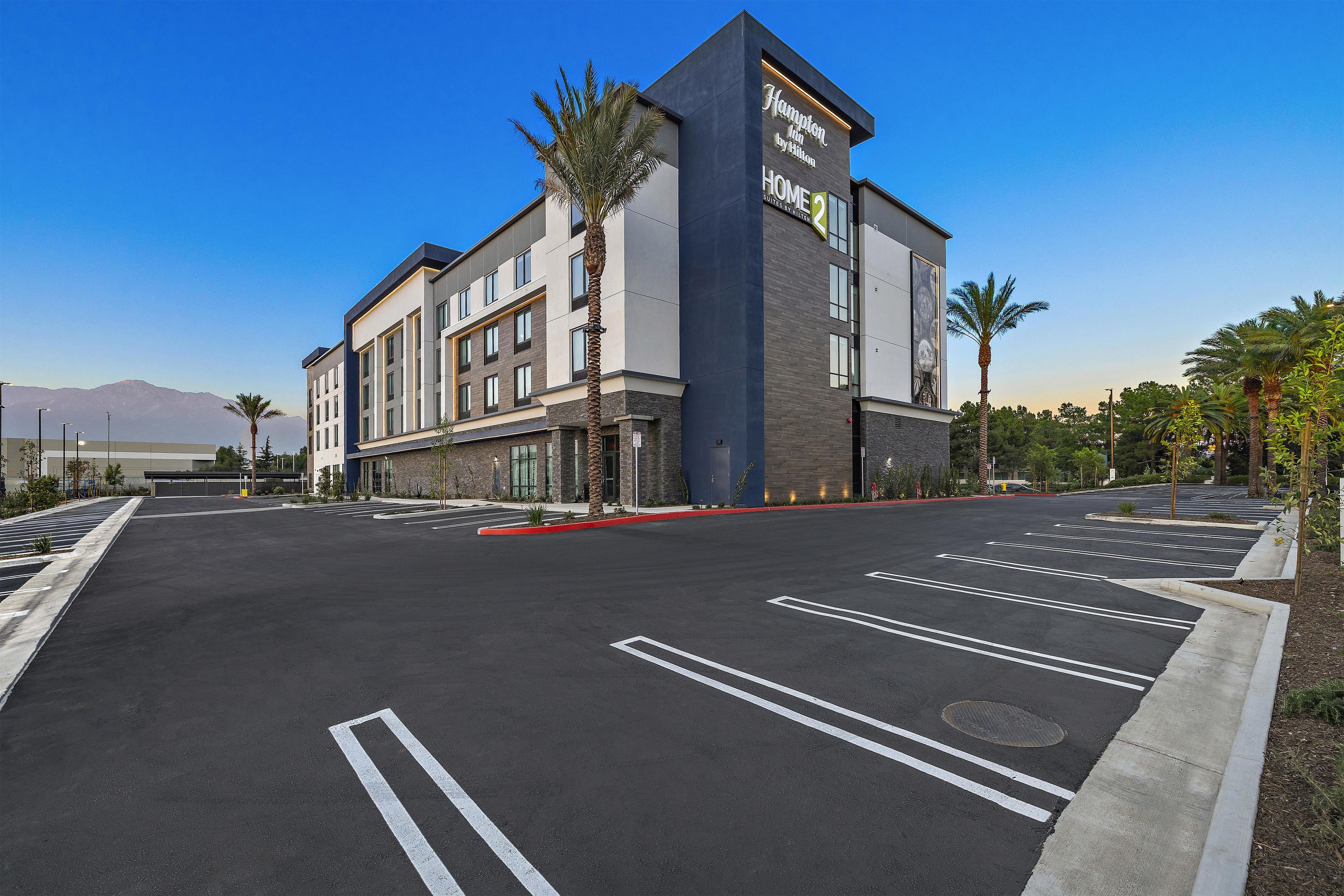 Un hôtel moderne doté d’un grand parking, d’une enseigne bien visible et offrant une vue dégagée sur les montagnes en arrière-plan.