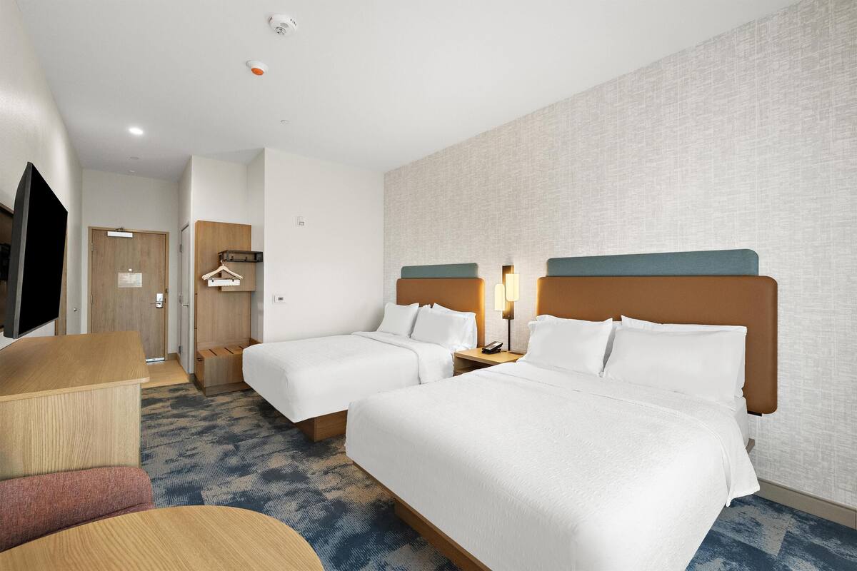 Een hotelkamer met twee bedden, een bureau, een televisie en een kledingkast.