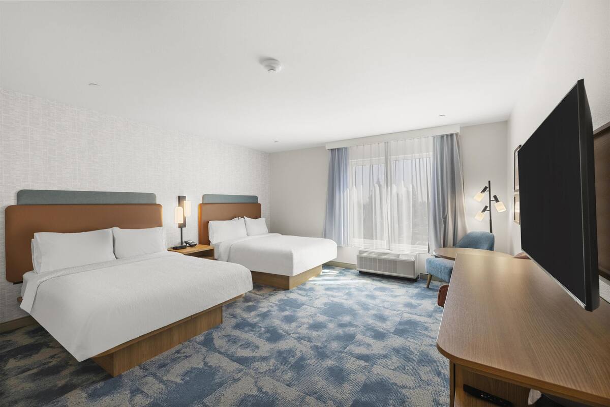 Een hotelkamer met twee bedden, een bureau, een televisie en een raam met gordijnen.