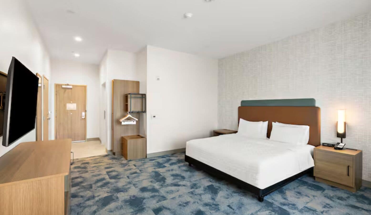 A hotel room with a bed, bedside tables, a TV, a wardrobe, and a mirror.