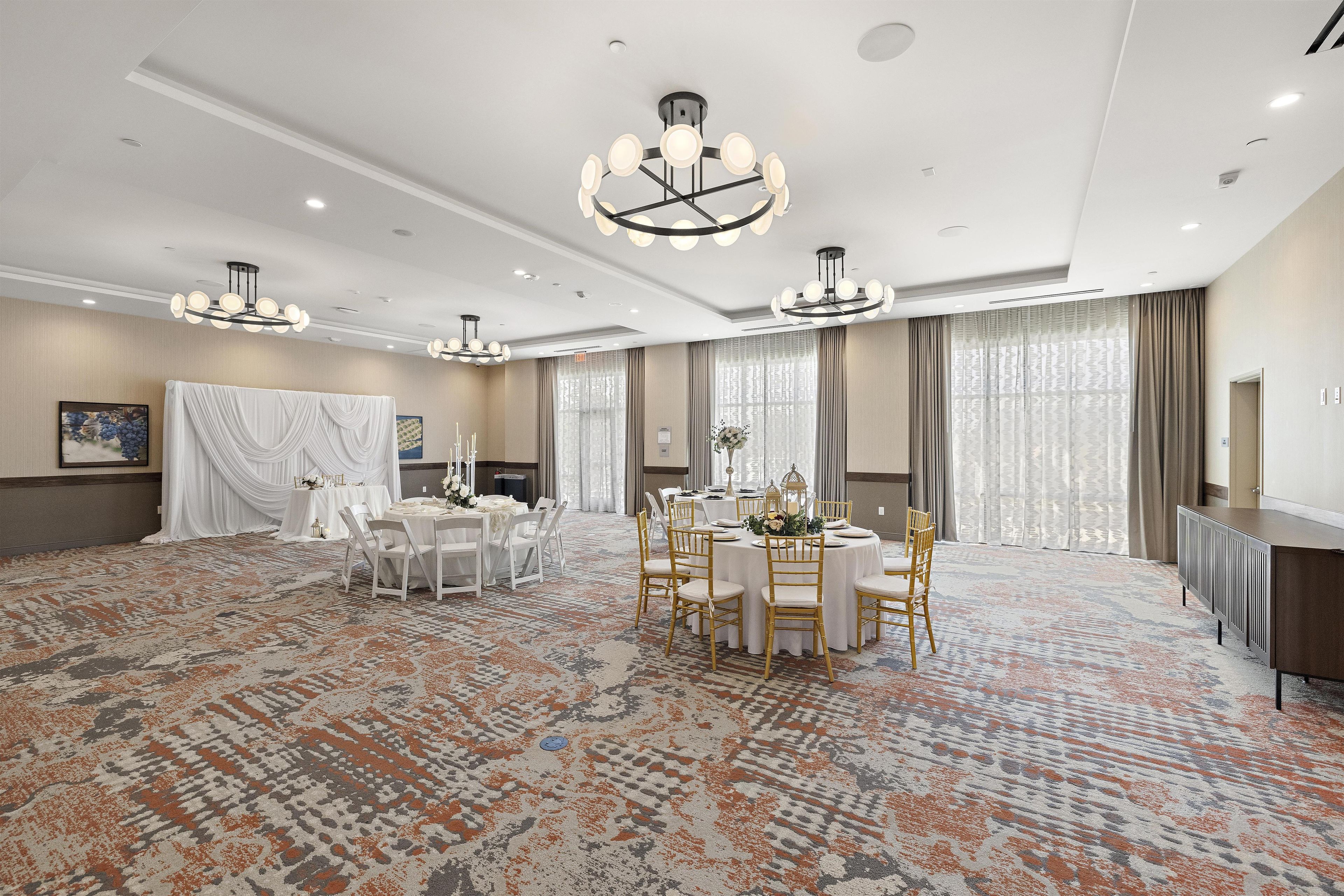 A spacious hotel dining area with round tables, white chairs, and a patterned carpet.