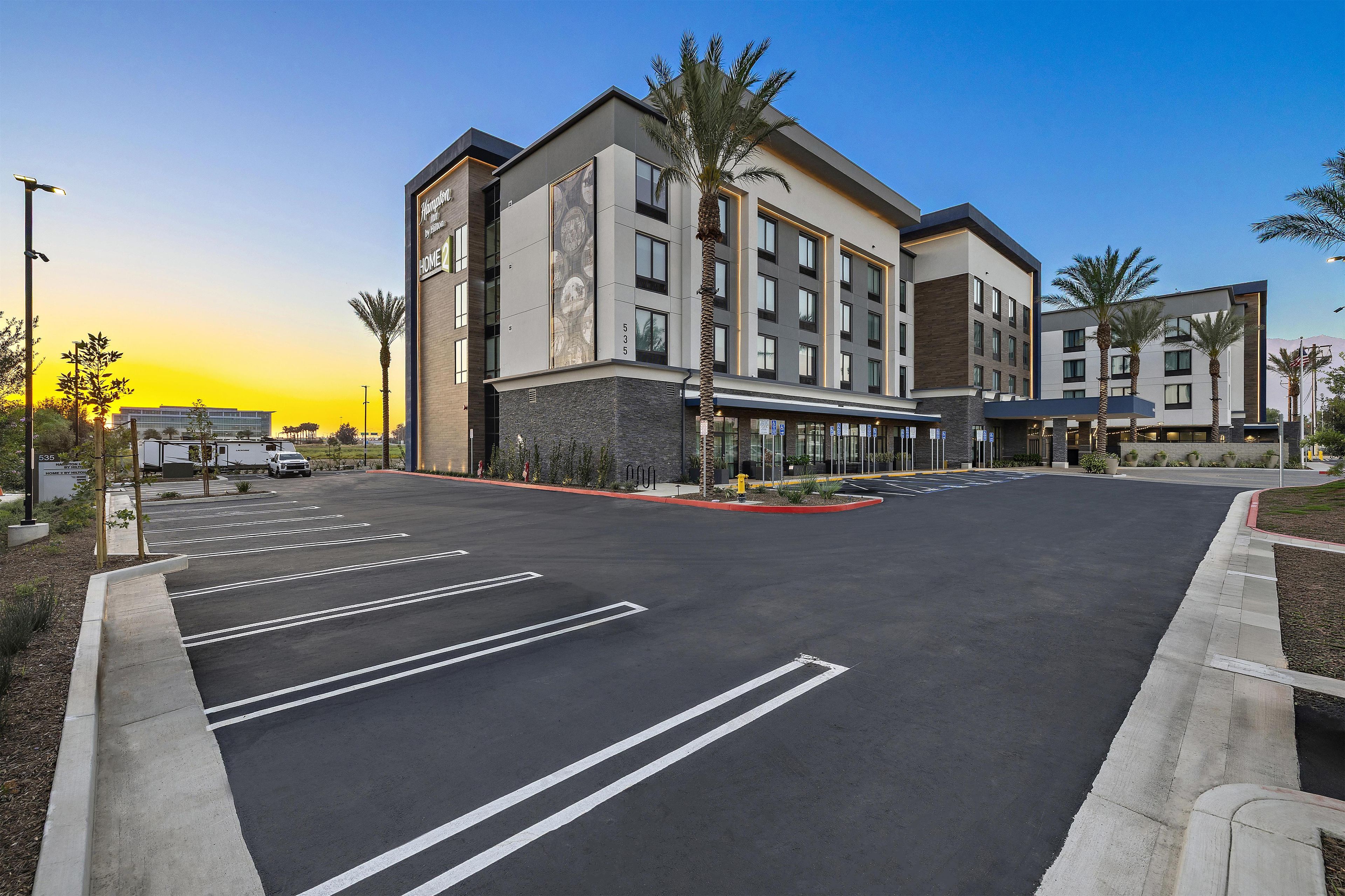 Un hôtel moderne doté d’un vaste parking, d’une entrée centrale et d’une grande fresque ornant la façade du bâtiment.