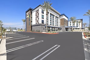A modern hotel with a parking lot, palm trees, and a clear blue sky. - Hampton Inn By Hilton Ontario Airport (Ontario)