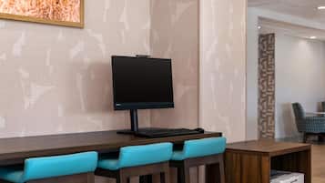 Un espace de travail dans une chambre d’hôtel, équipé d’un écran plat, d’un clavier et d’une imprimante, le tout posé sur une table en bois.
