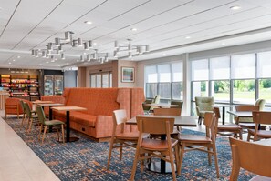 A modern dining area with orange seating, wooden tables, and chairs. - Hampton Inn & Suites Cadillac (Cadillac)