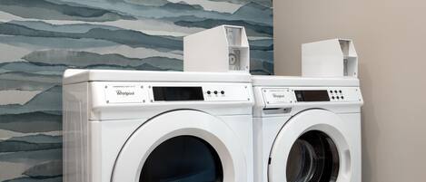 Twee voorlader wasdrogers van Whirlpool voor professioneel gebruik in een wasserij met een patroon op de muur.