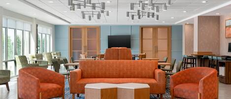 Un área de estar moderna con un sofá, sillones, una mesa de centro y un televisor de pantalla plana.