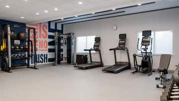 Un gimnasio con cintas de correr, máquinas de pesas y pesas sueltas.