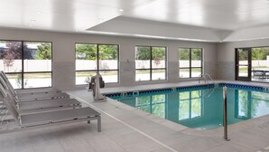 A modern indoor swimming pool with clear glass walls, a pool ladder, and a few lounge chairs. - Hampton Inn & Suites Cadillac (Cadillac)
