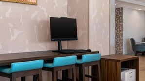 Un'area di lavoro in hotel con un monitor a schermo piatto, tastiera e stampante su un tavolo di legno.