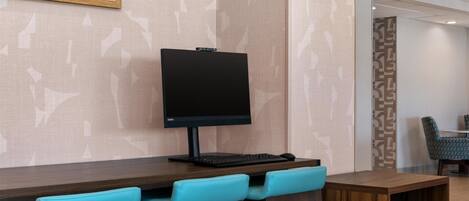 Un espacio de trabajo en un hotel con monitor de pantalla plana, teclado e impresora sobre una mesa de madera.