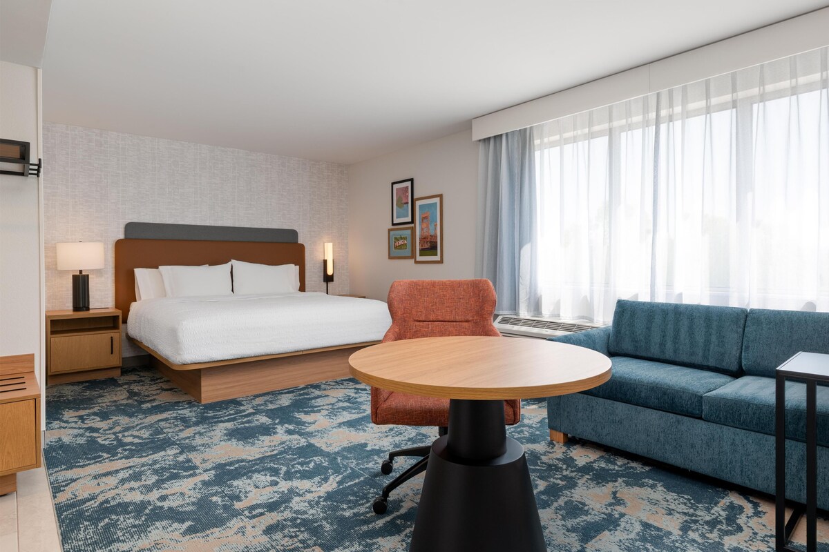 A hotel room with a bed, a sofa, a chair, a small table, and a window with curtains.