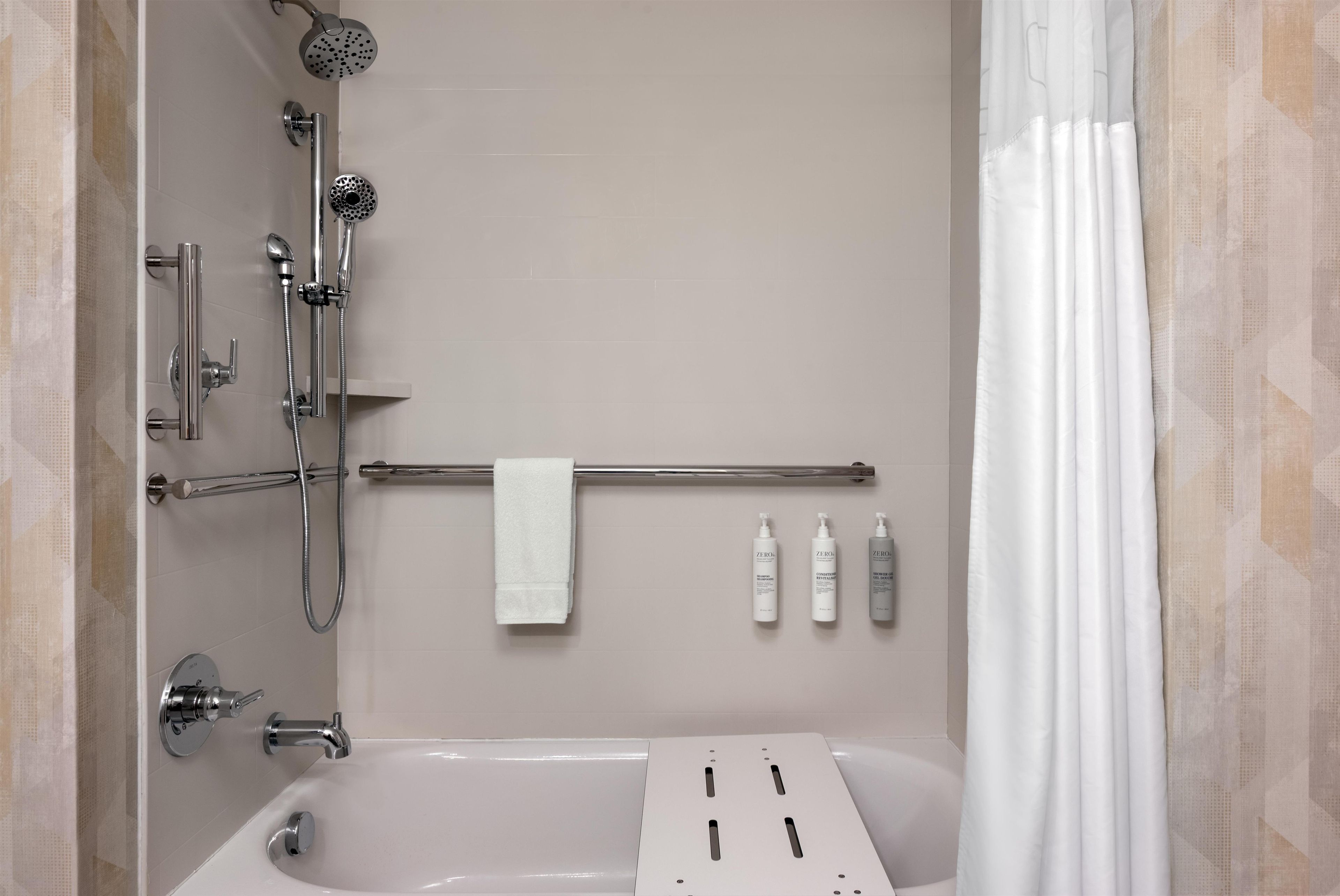 A bathroom with a bathtub, a shower with a handheld showerhead, a towel rack with a towel, and three bottles of shampoo.