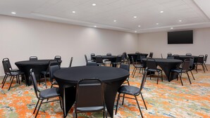 Una sala conferenze con diversi tavoli e sedie, un televisore a schermo piatto appeso al muro e un tappeto decorato.
