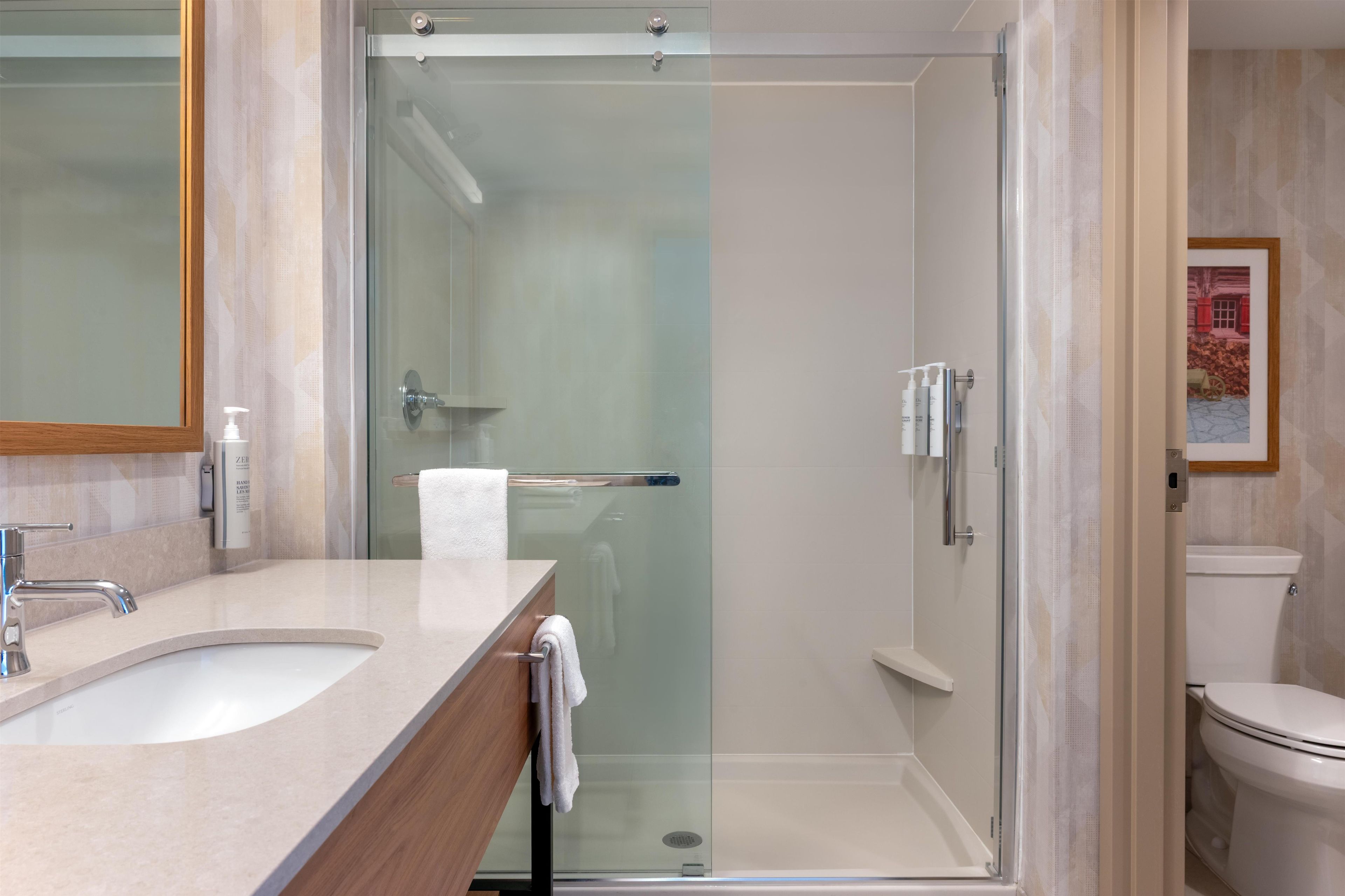 Un baño moderno con ducha envuelta en vidrio, un lavabo con tocador de madera y un inodoro.