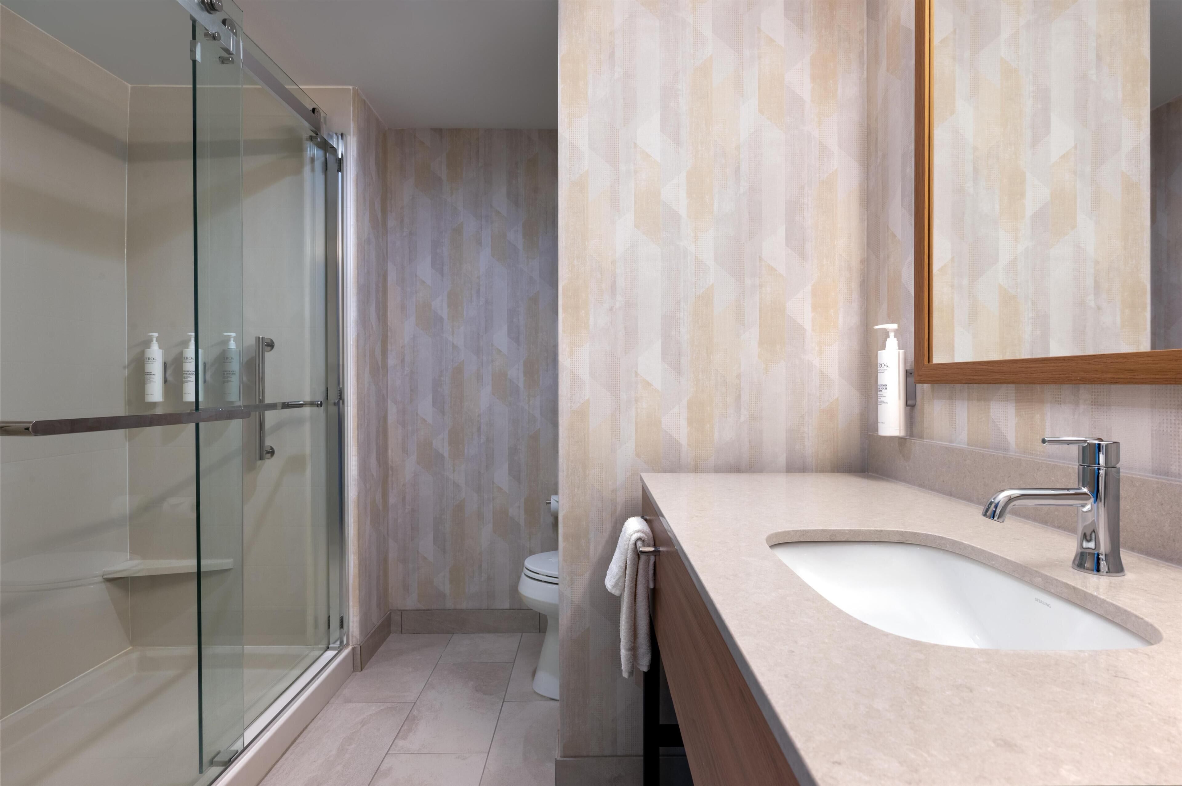 A modern bathroom with a glass shower enclosure, a toilet, and a sink with a mirror.
