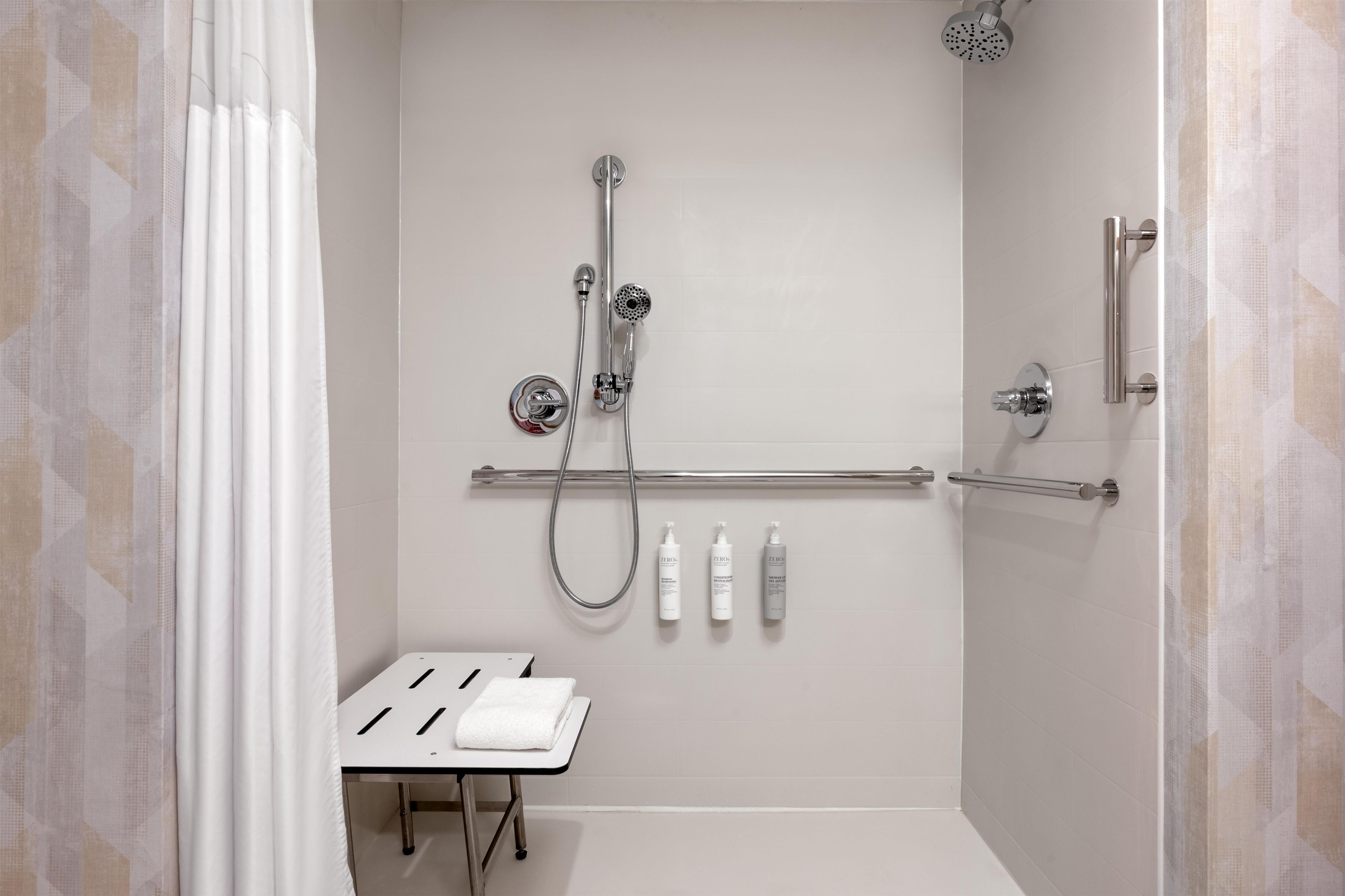A modern shower area with a handheld showerhead, a wall-mounted faucet, and a handheld showerhead. There are three bottles of shampoo and conditioner on the wall.