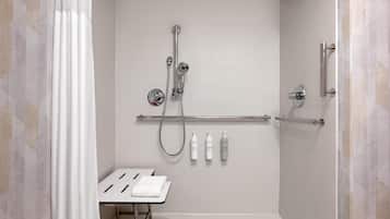 A modern shower area with a handheld showerhead, a wall-mounted faucet, and a handheld showerhead. There are three bottles of shampoo and conditioner on the wall.