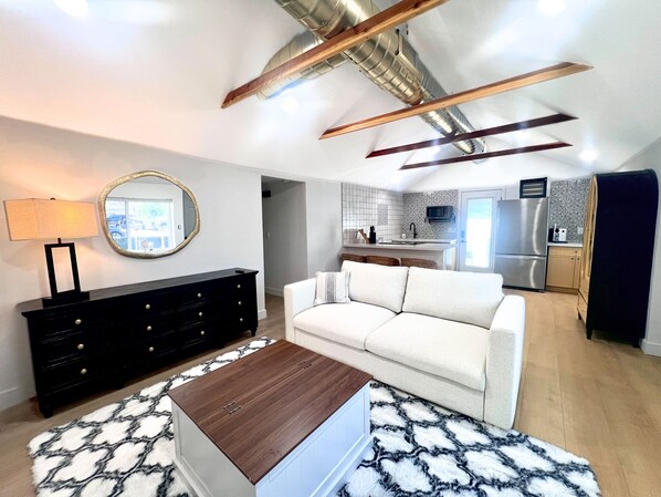 Una sala de estar moderna con un sofá, una mesa de centro de madera, un aparador negro y una alfombra estampada.