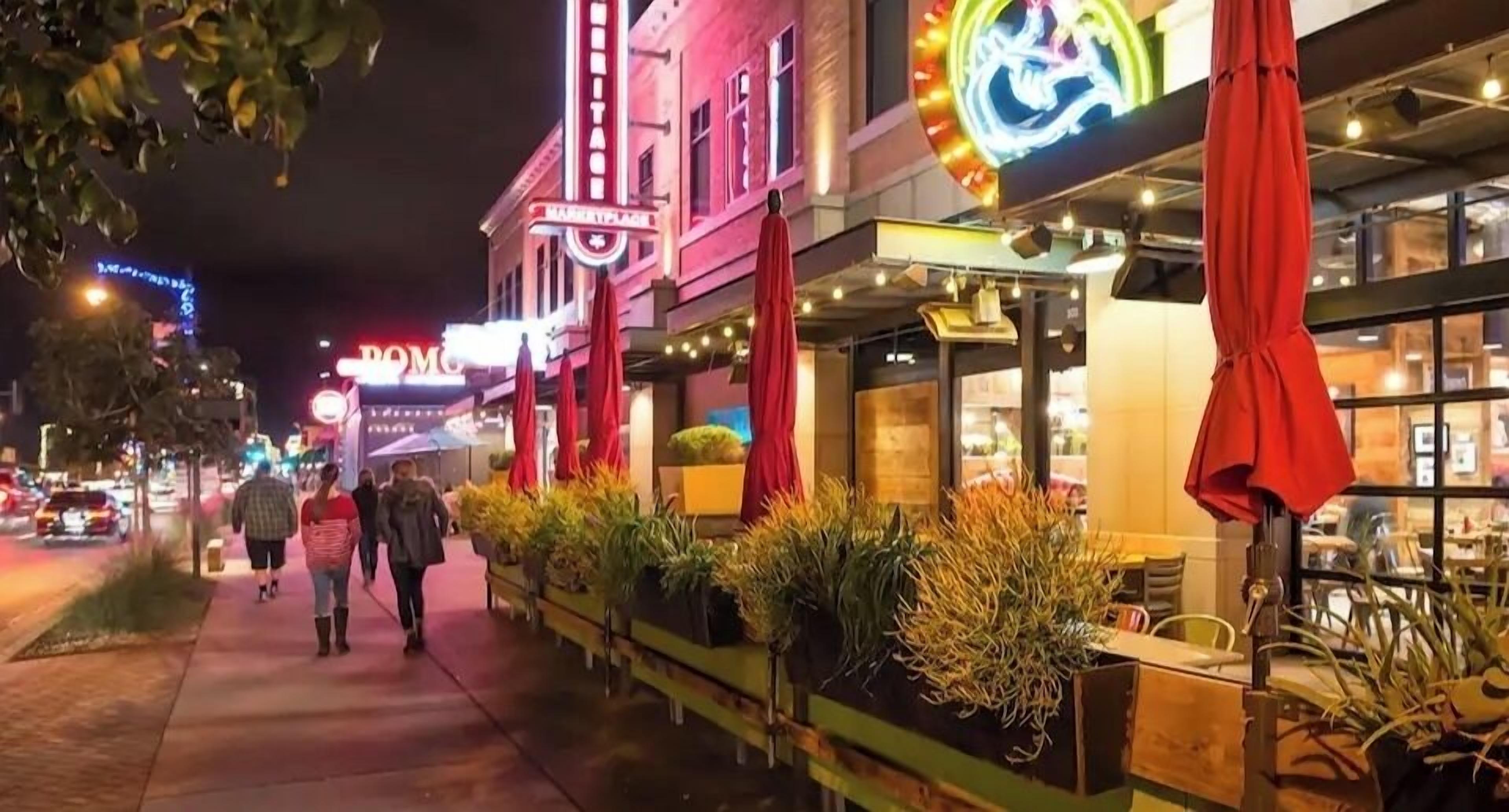 Une rue bordée d’un théâtre aux néons éclatants et de terrasses agrémentées de plantes en pot.