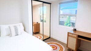 A bedroom with a bed, a wardrobe, a desk, and a window with a view of greenery. - Cozy Cottage in Downtown Gilbert Heritage District Sleeps Up To 3 (Gilbert)