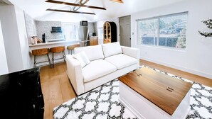 A modern living room with a white sofa, a wooden coffee table, and a kitchen in the background. - Cozy Cottage in Downtown Gilbert Heritage District Sleeps Up To 3 (Gilbert)