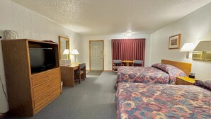A hotel room with a TV, desk, two beds, a chair, and a table. - North Winds Lodge LLC (Bowman)