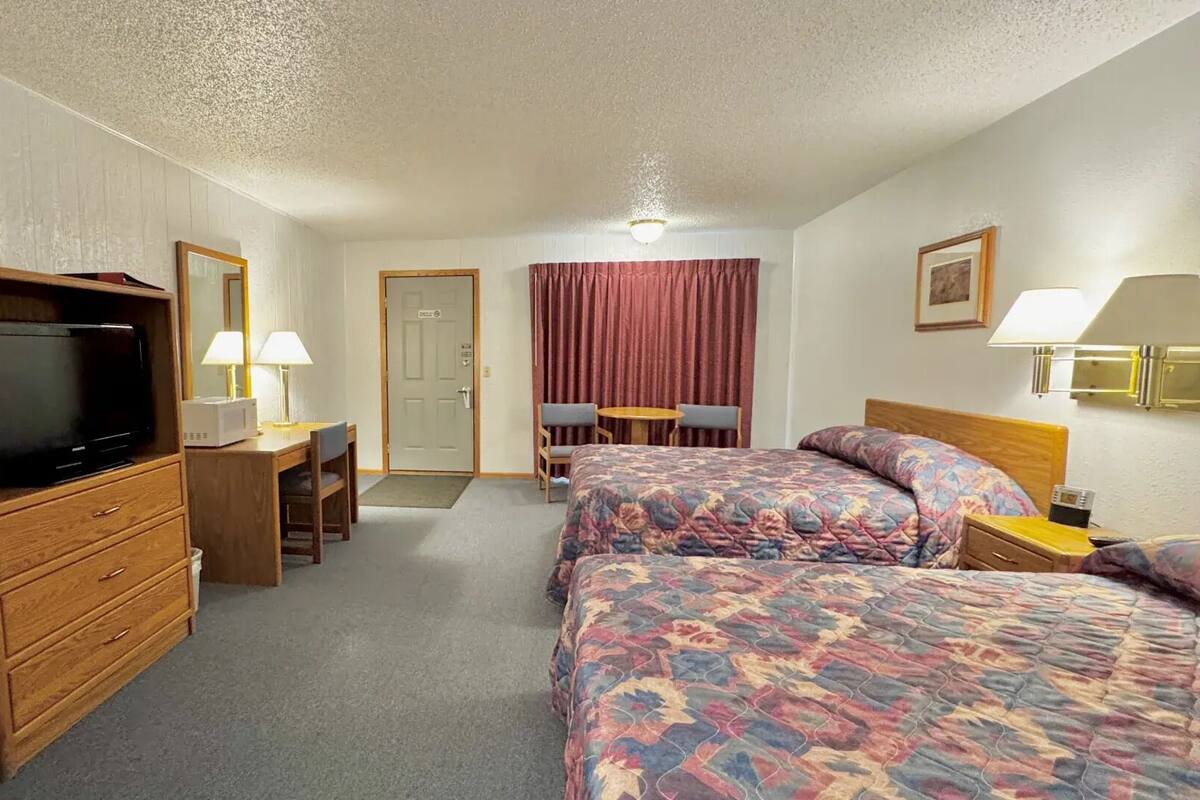 A hotel room with a TV, desk, two beds, a chair, and a table.