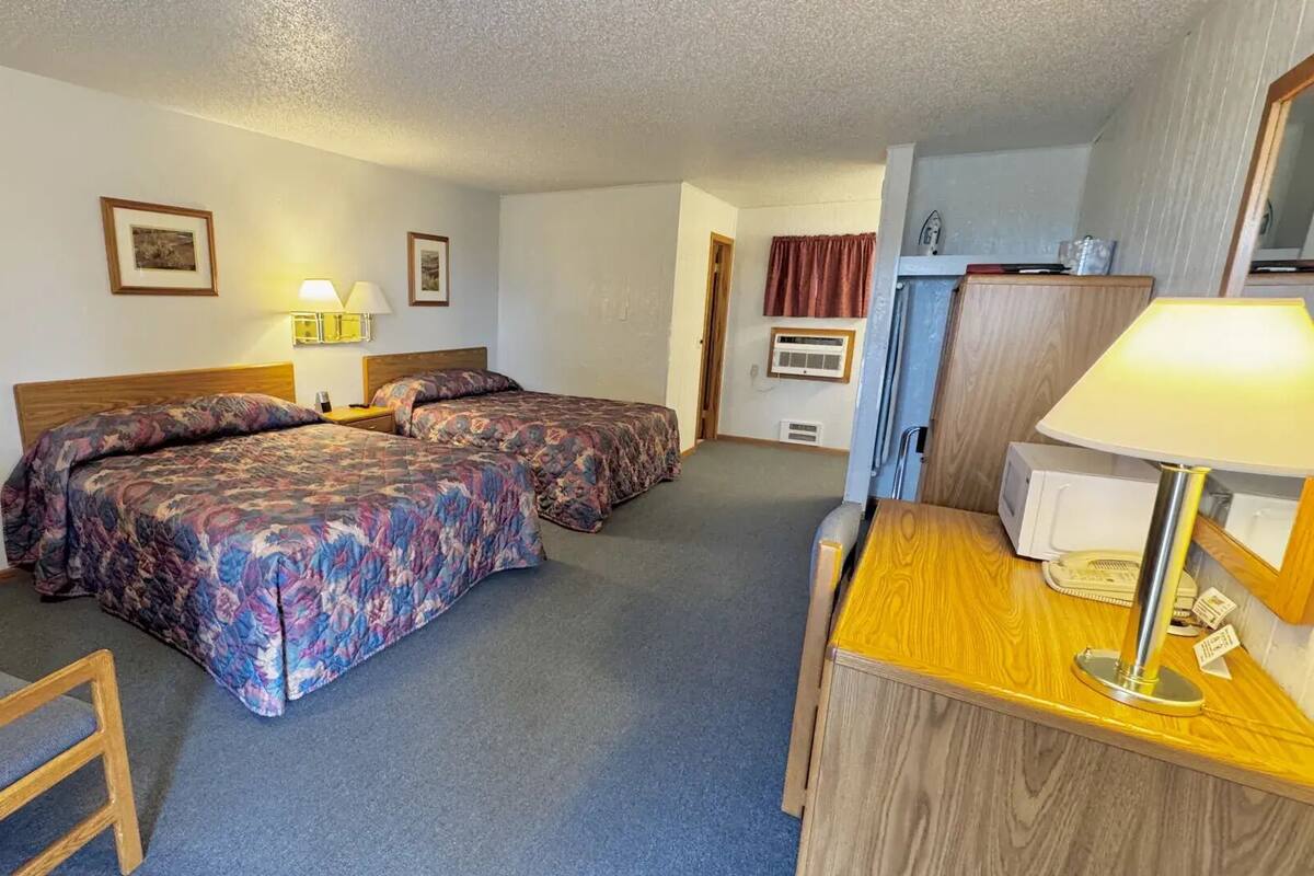 A hotel room with two beds, a desk, a chair, a lamp, and a mirror.
