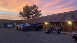 A building with a gravel parking area and several parked vehicles, including cars and motorcycles. - North Winds Lodge LLC (Bowman)