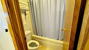 A small bathroom with a toilet, a shower curtain, and a wooden door. - North Winds Lodge LLC (Bowman)