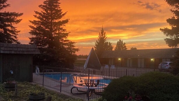 A swimming pool with a fenced deck, surrounded by trees and a gravel area. - North Winds Lodge LLC (Bowman)