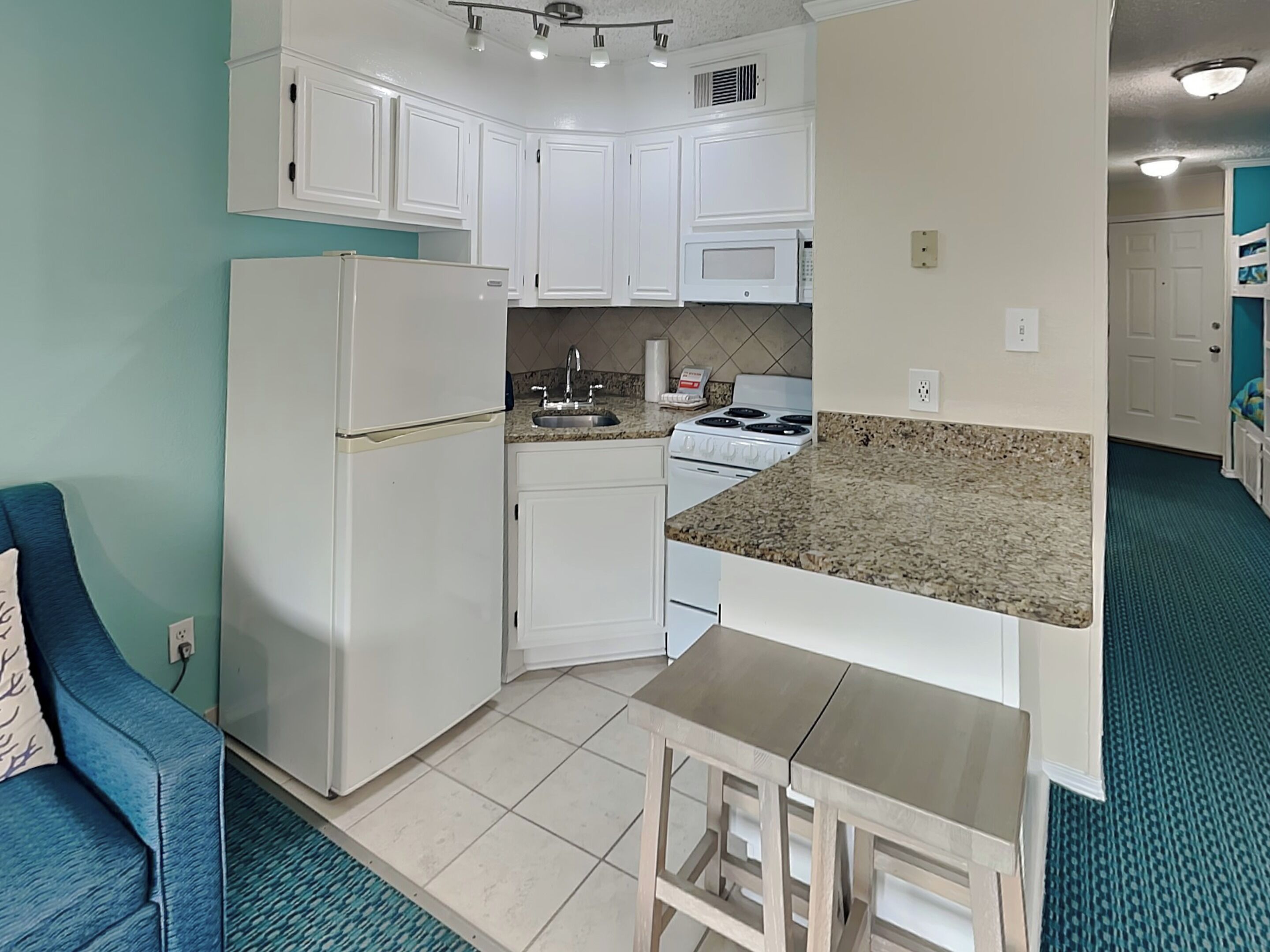 A compact kitchen with white cabinets, a built-in microwave, a stove, and a small dining area with a bench.