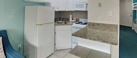 A compact kitchen with white cabinets, a built-in microwave, a stove, and a small dining area with a bench.