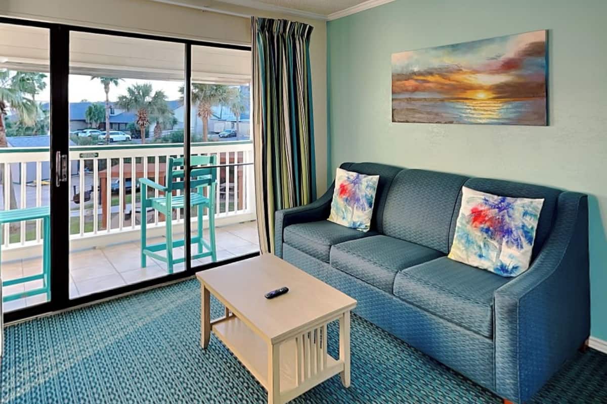 A living room with a sofa, two chairs, a coffee table, and a painting on the wall.
