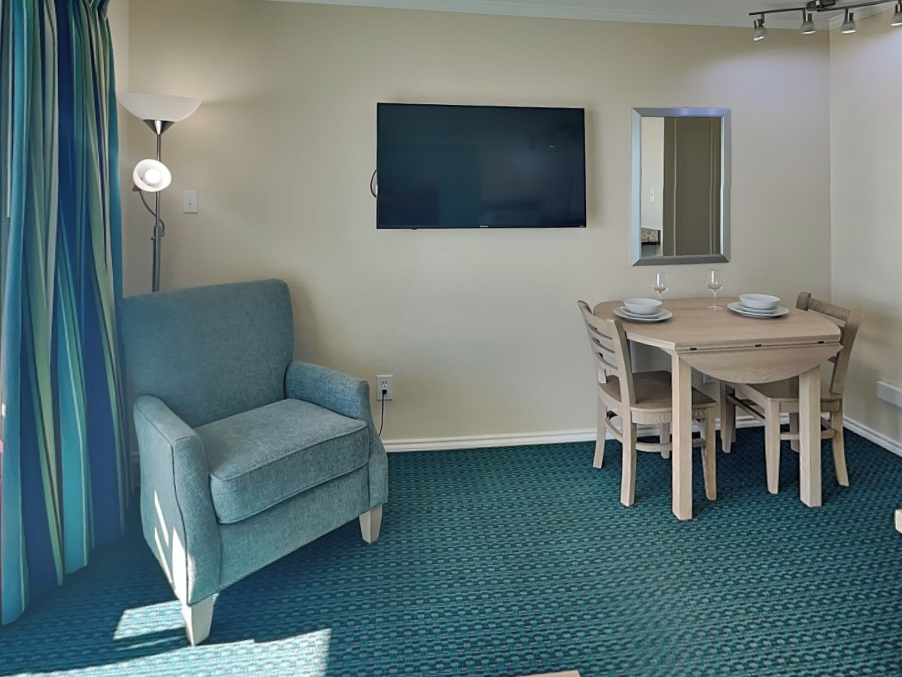 Ein Zimmer mit blauem Sessel, einem Esstisch mit Stühlen, einem Flachbildfernseher und einem Spiegel an der Wand.