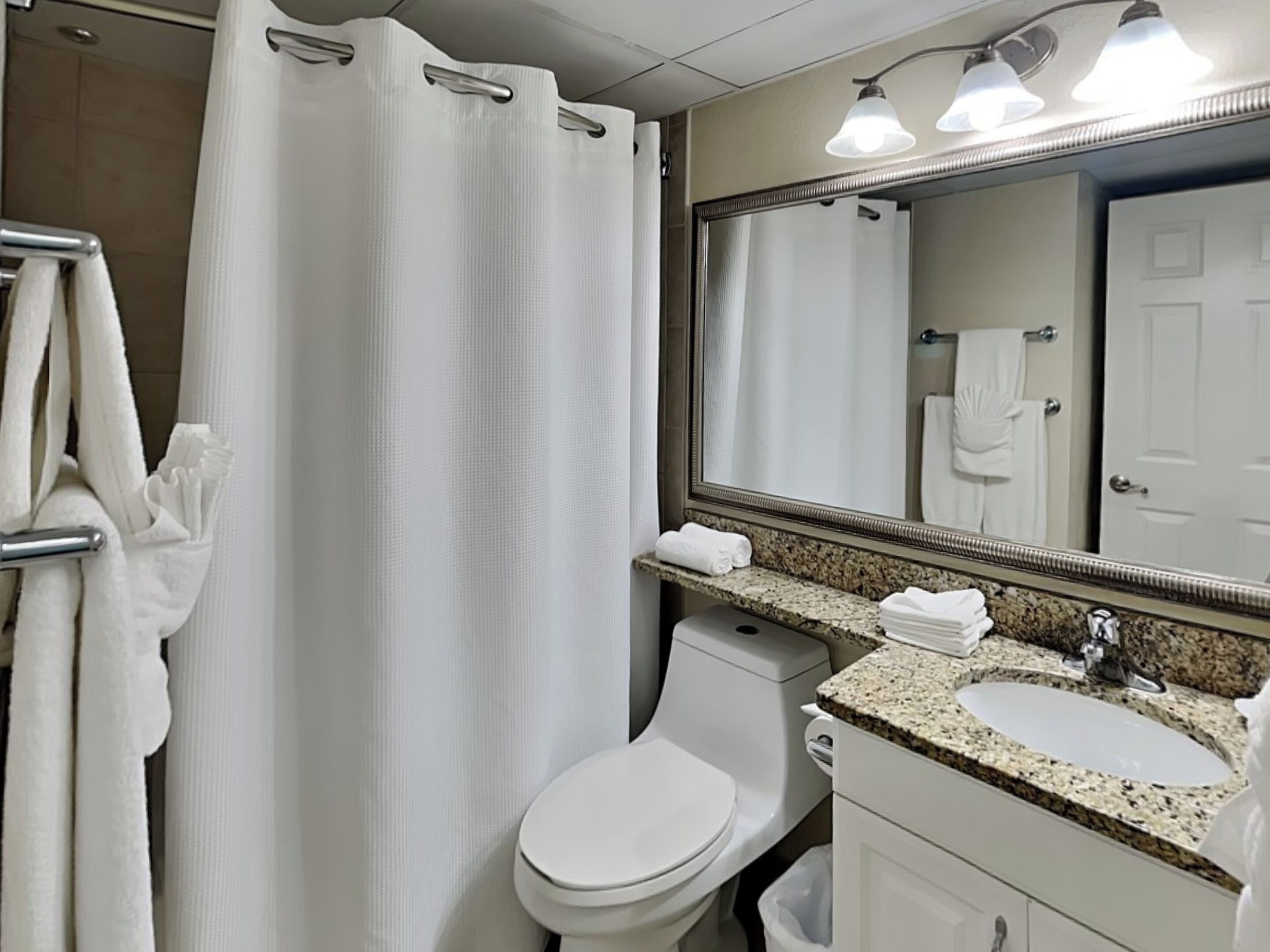 A bathroom with a shower curtain, a toilet, a sink, and a mirror.
