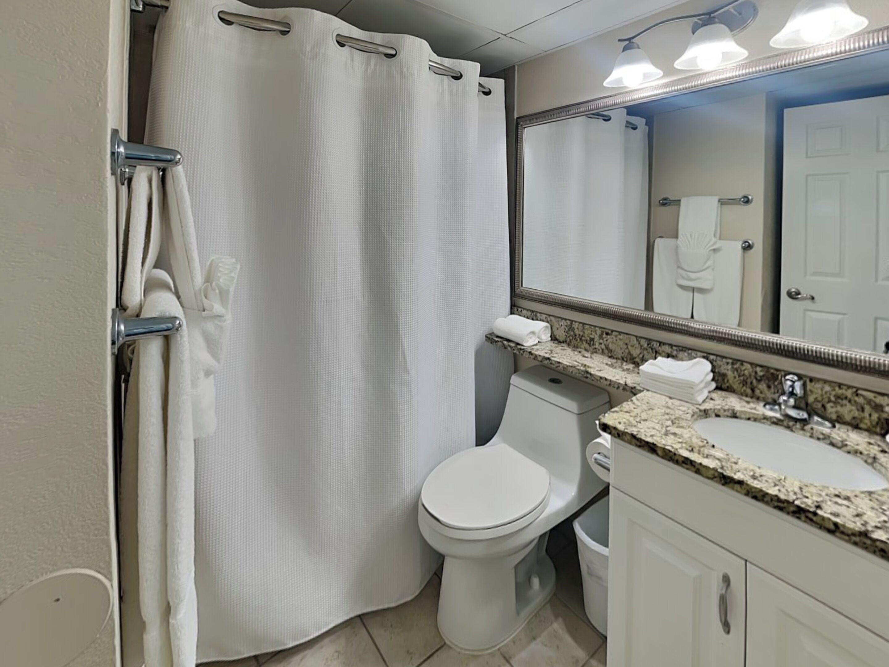 A bathroom with a shower curtain, toilet, sink, and mirror.