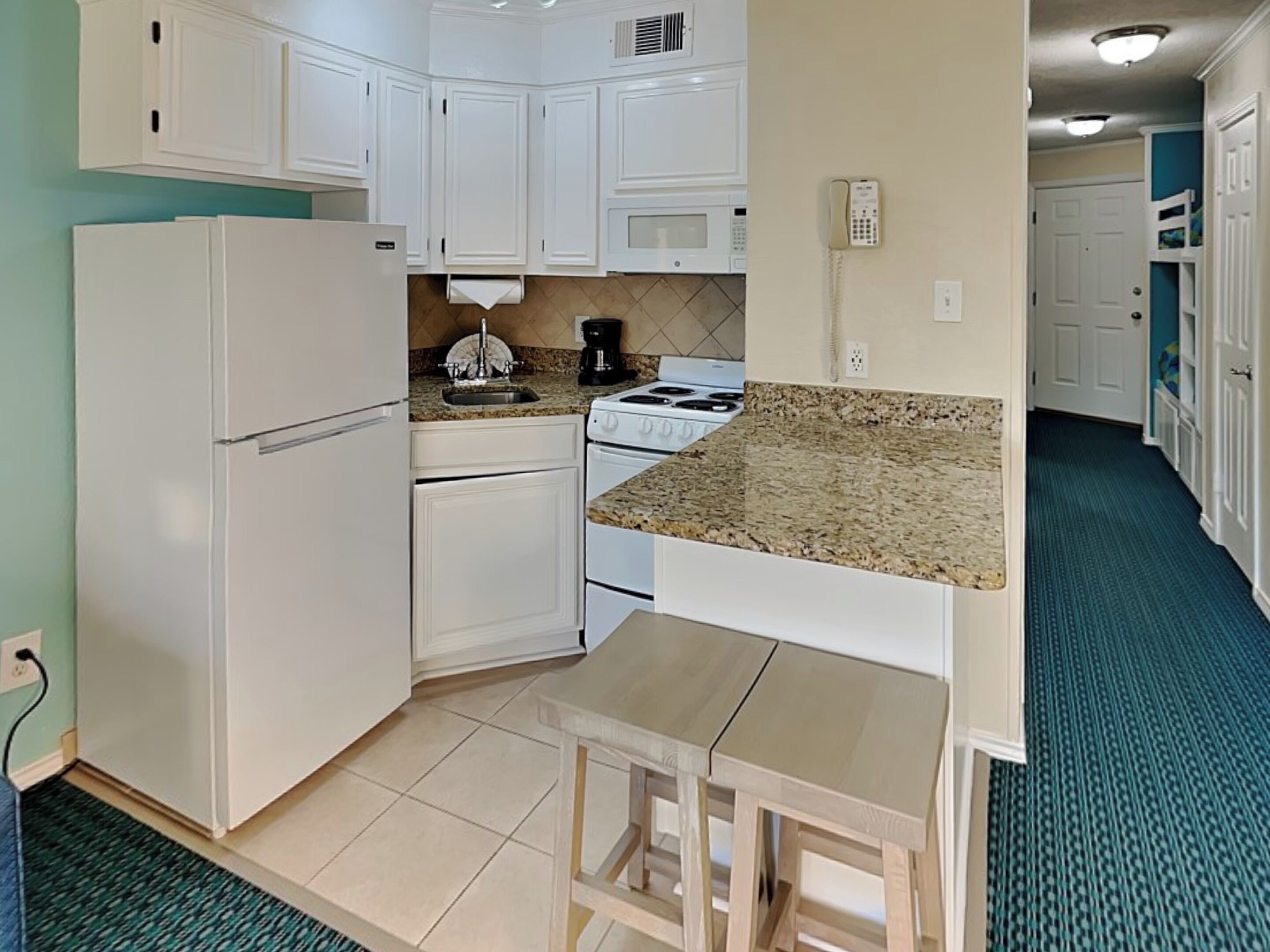 A compact kitchen with white cabinetry, a granite countertop, a stove, and a refrigerator.