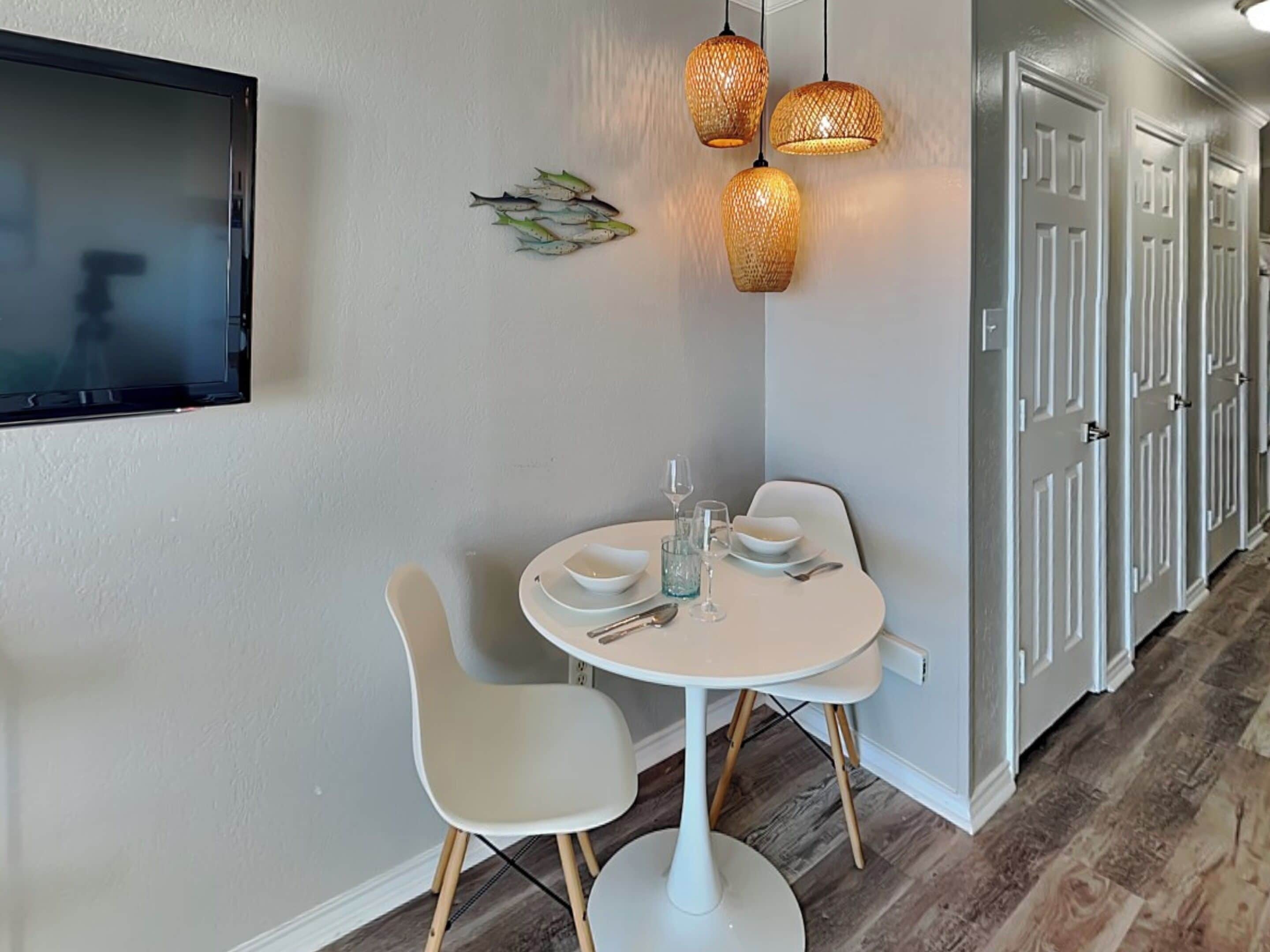 A dining area with a round table, two chairs, and a wall-mounted TV.